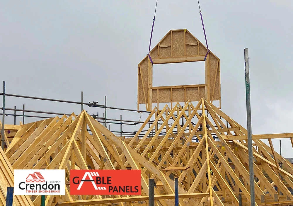 Gable panel lifted into the air by a crane above a roof under construction
