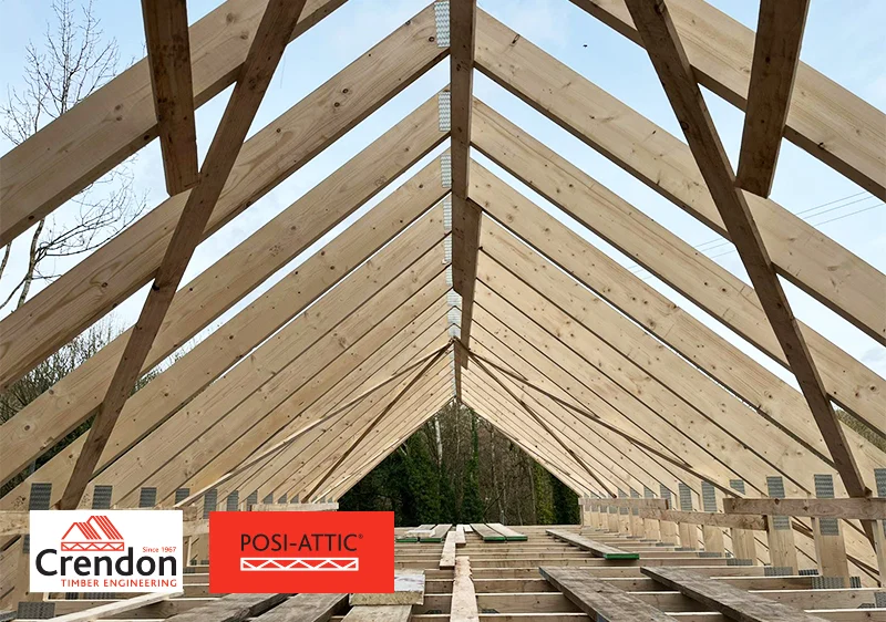 Exposed timber roof trusses forming a pitched frame at a construction site, with Posi-Attic and Crendon logos.